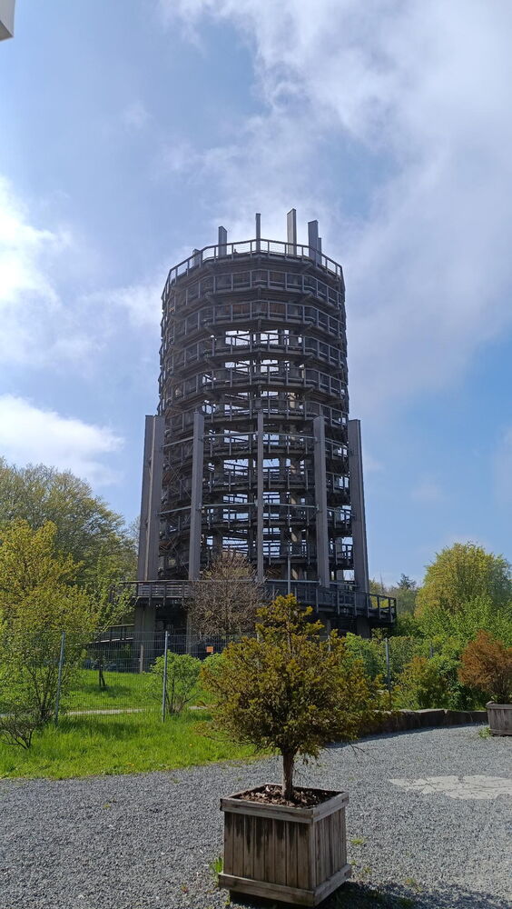 In einer grünen Landschaft bei blauem Himmel ist ein großer metallener Aussichtsturm zu sehen.